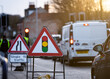 Temporary traffic lights triangle warning sign and traffic light showing red stop signal in background with queuing traffic jam at roadworks on sunny summer day