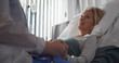© nimito - Close up of doctor holding hand and talking to sick aged female patient in hospital ward