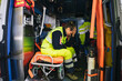 Portrait of paramedic in an ambulance sitting on a litter, with his hand on his forehead, exhausted by the intense first aid service for the Covid-19 Coronavirus pandemic - Millennial volunteer rests