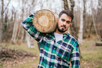 Young Caucasian male with a beard carrying a tree trunk in a forest