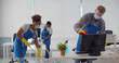 Team of diverse young cleaning service professionals in safety mask at work in office