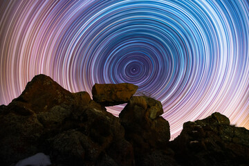 Wall Mural - the rocks silhouette on the hill under the colorful star trails on the sky. night timelapse photogra