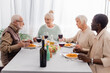 © LIGHTFIELD STUDIOS - happy multicultural and senior friends talking while having delicious lunch near glasses of red wine