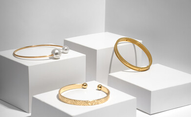 Three modern golden bracelets on white geometric boxes