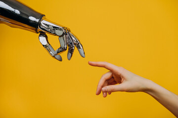 Robotic bionic hand and a woman's hand pulling fingers together on a yellow background close-up, the concept of human interaction and modern technology