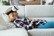 © nenetus - Beautiful young woman using virtual reality headset and enjoying the moment lying on couch at home.