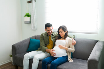 Wall Mural - Attractive husband and prgnant wife hugging while resting on the couch