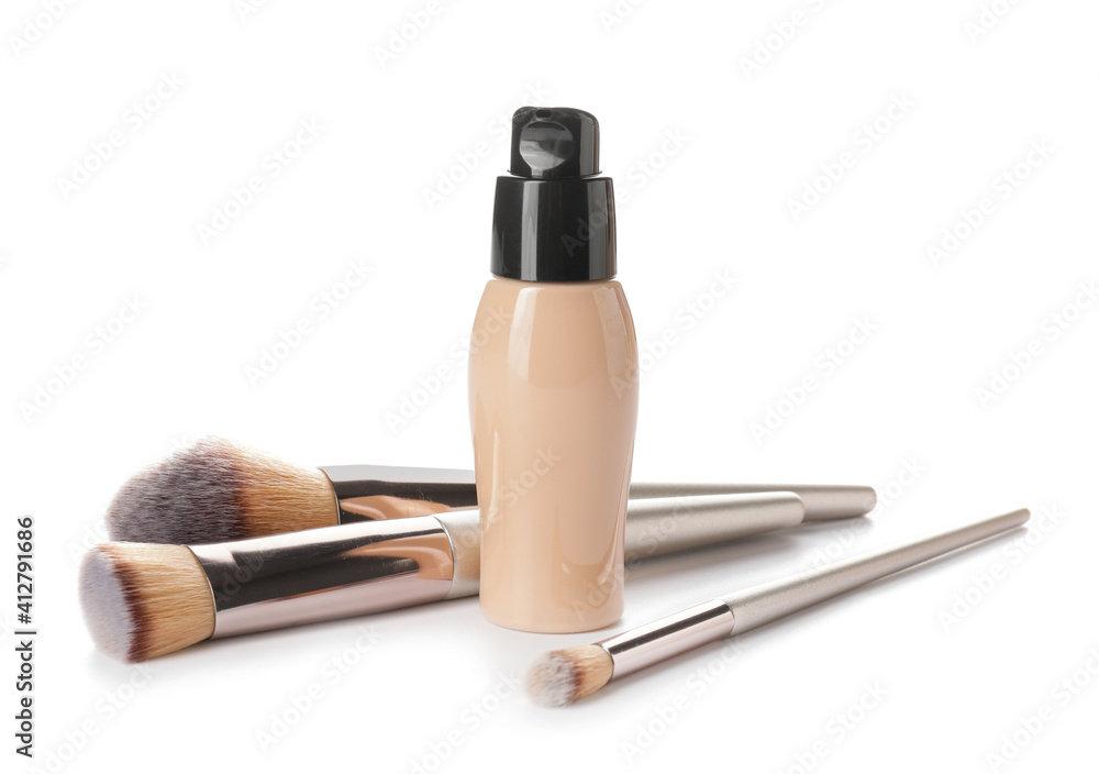 Bottle of makeup foundation and brushes on white background