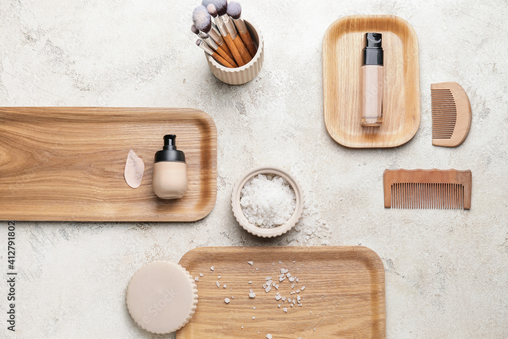 Bottles of makeup foundation, brushes and hair combs on light background