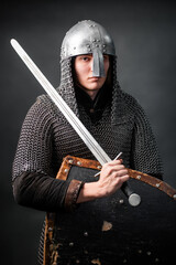 Portrait of a medieval warrior of the late Viking era and the beginning of the Crusades. Knight in chain mail and helmet armed with a shield and sword isolated on a dark background.