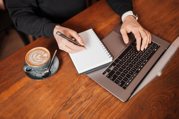 Handsome man working on laptop in the workplace. Businessman typing information on computer at work table with coffee and notepad