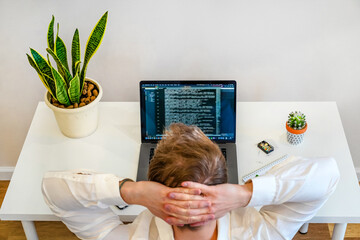 Wall Mural - a male programmer works with a laptop. the man is resting, sitting with hands behind head