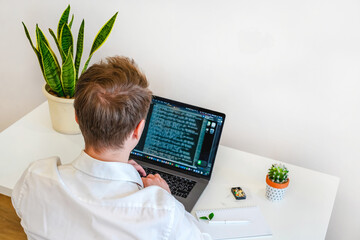 Wall Mural - a male programmer works in front of a laptop screen in a bright office or remotely from home. workpl