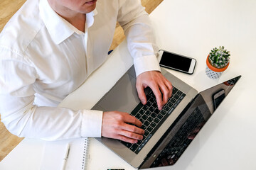 Wall Mural - A male programmer works in front of a laptop screen in a bright office or remotely from home. Workplace