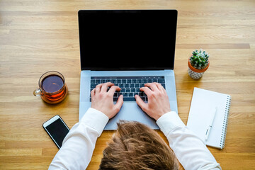 Wall Mural - a male programmer works in front of a laptop screen in a bright office or remotely from home. workpl