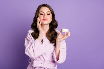 Sticker - Photo portrait of girl with closed eyes applying cream from open jar with fingers isolated on vivid purple colored background