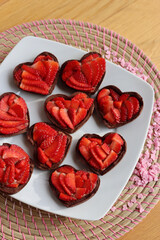 Wall Mural - Valentine’s day dessert background. Mini heart shaped chocolate tarts with fresh strawberries on a plate on a wooden table