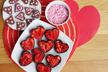 Wall Mural - Valentine’s day dessert background. Mini heart shaped chocolate tarts with fresh strawberries and glazed ccokies with sprinkles on a wooden table