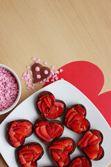 Wall Mural - Valentine’s day dessert background. Mini heart shaped chocolate tarts with fresh strawberries and glazed ccokies with sprinkles on a wooden table