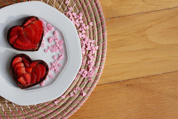 Wall Mural - Valentine’s day dessert with copy space. Mini heart shaped chocolate tarts with fresh strawberries on a plate on a wooden table