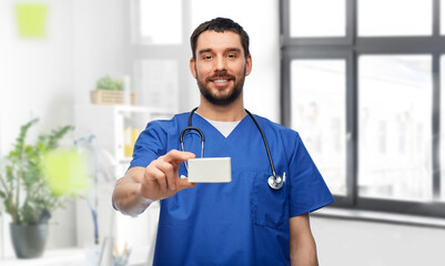 Poster - healthcare, profession and medicine concept - doctor or male nurse in blue uniform with box of pills and stethoscope over medical office at hospital background