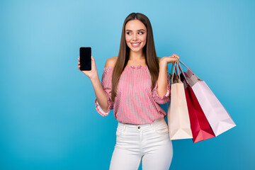 Sticker - Portrait of lovely cheerful girl holding in hand cell carrying new clothes isolated over bright blue color background