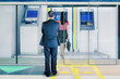 © Creativa Images - Two business people queue to withdraw money at ATM