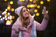 © New Africa - Happy young woman taking selfie outdoors in evening. Christmas celebration