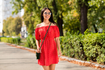 Sticker - Photo portrait of female student smiling wearing stylish red dress in summer hot weather sunglasses walking in green park