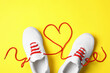 Stylish sneakers and red shoe laces in shape of heart on yellow background, flat lay