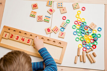 child playing with different color wooden rings. sequence, fine motor skills, therapy task for educa