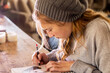 © Mint Images - Teenage girl in a woolly hat drawing with a pencil on a sketchpad.