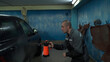 © Nicolaos - A Caucasian man works in a car wash service. A man in a worker's uniform washes the car thoroughly by spraying it with a water pistol.