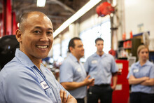 Portrait Of Smiling Pacific Islander Repair Shop Owner With Team In The Background