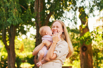 adorable baby kissing her mom, young happy laughing mother in summer park