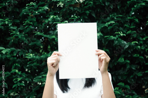 Woman Holding Paper In Front Of Face Against Plants