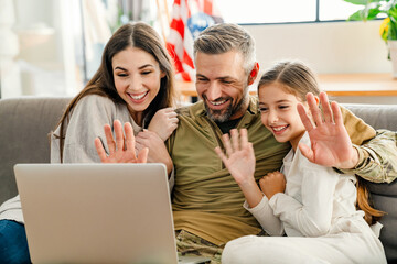 Wall Mural - Happy military man waving hand with his family while using laptop