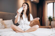 © Ivan - woman drinks milk from a bottle while sitting on the bed. model in silk pajamas with a bottle of milk. Female in white silk pajamas with a bottle of milk. morning or evening in the bedroom