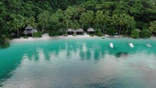 Boats Near Ocean Beach With Huts Among Palm Trees In Triton Bay, Raja Ampat. Stunning View From Drone On Water Transport In Turquoise Lagoon Near Tropical Resort Papua, Indonesia.