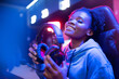 © Parilov - Headphones with microphone in hands of young african happy woman professional gamer online video game, neon background