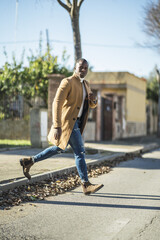 Wall Mural - Shallow focus shot of a stylish handsome African male in a coat crossing the road