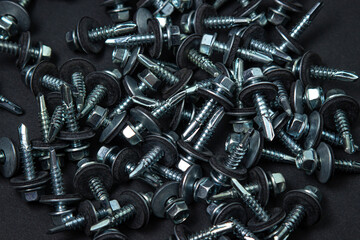 Roofing screws on a black background. Metal building material. Self-tapping screws for metal