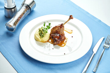 Wall Mural - Duck leg confit with sweet sauce garnished with mashed potatoes in a white plate on a blue tablecloth