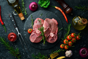 Meat. Lamb steak on the bone with rosemary and spices. On a black stone background. Top view.