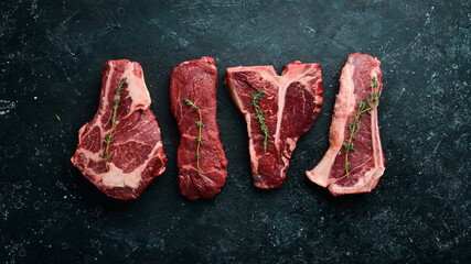 Set of raw steaks - t-bone, tomahawk, striploin, tenderloin, new york steak. On a black stone background. Top view.