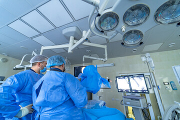 Doctors in clinic with big operation lamps on the ceiling. Operation room interior with medics in scrubs. View from the back.