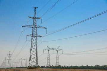 High voltage towers with electricity transmission power lines in field on sunny day