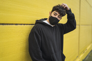 Wall Mural - Handsome European skater in hoodie posing in front of a yellow wall in a facial - new normal concept