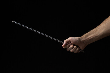 Long drill on a black background. A man's hand holds a long drill. Construction tool