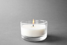 Burning Small Wax Candle In Glass Holder On Grey Background